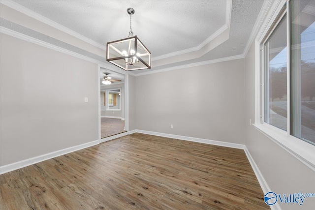 unfurnished dining area with ceiling fan with notable chandelier, a textured ceiling, hardwood / wood-style flooring, a tray ceiling, and crown molding