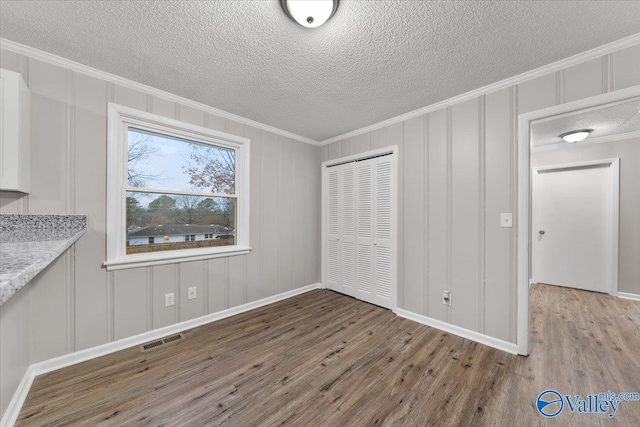 unfurnished dining area featuring a textured ceiling, crown molding, and wood-type flooring