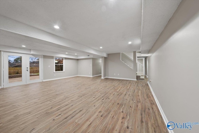 basement with a textured ceiling, light hardwood / wood-style flooring, and french doors