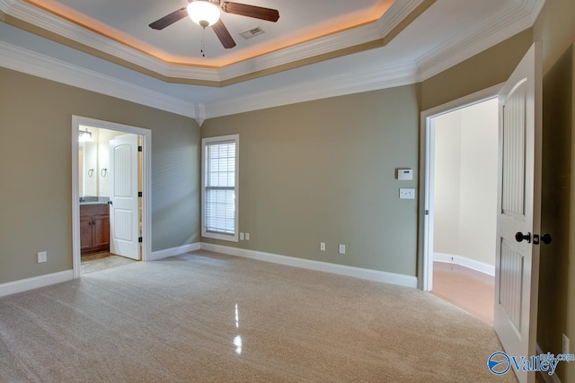 unfurnished bedroom featuring ensuite bath, ceiling fan, crown molding, a tray ceiling, and light carpet