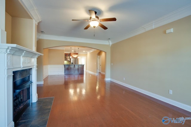 unfurnished living room with a tiled fireplace, ceiling fan, dark hardwood / wood-style flooring, and ornamental molding