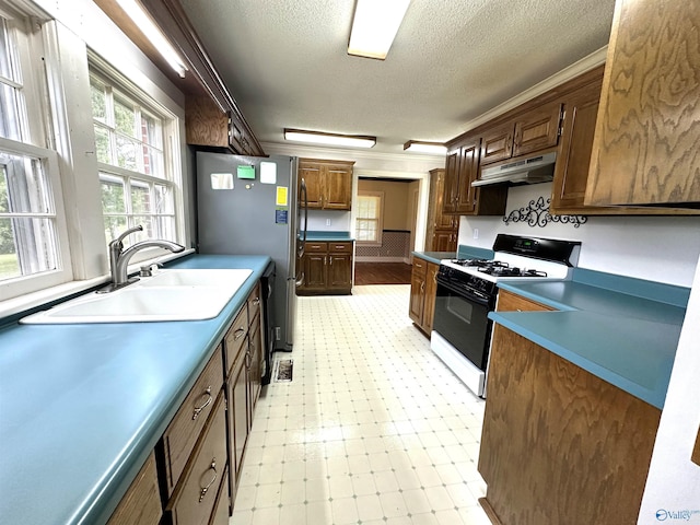 kitchen featuring sink, a textured ceiling, stainless steel refrigerator, ornamental molding, and gas range oven