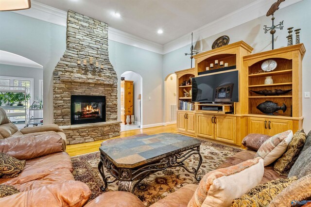 living room with light wood-type flooring, crown molding, and a stone fireplace