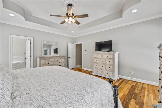 bedroom with ceiling fan, light wood-type flooring, a raised ceiling, and ensuite bath