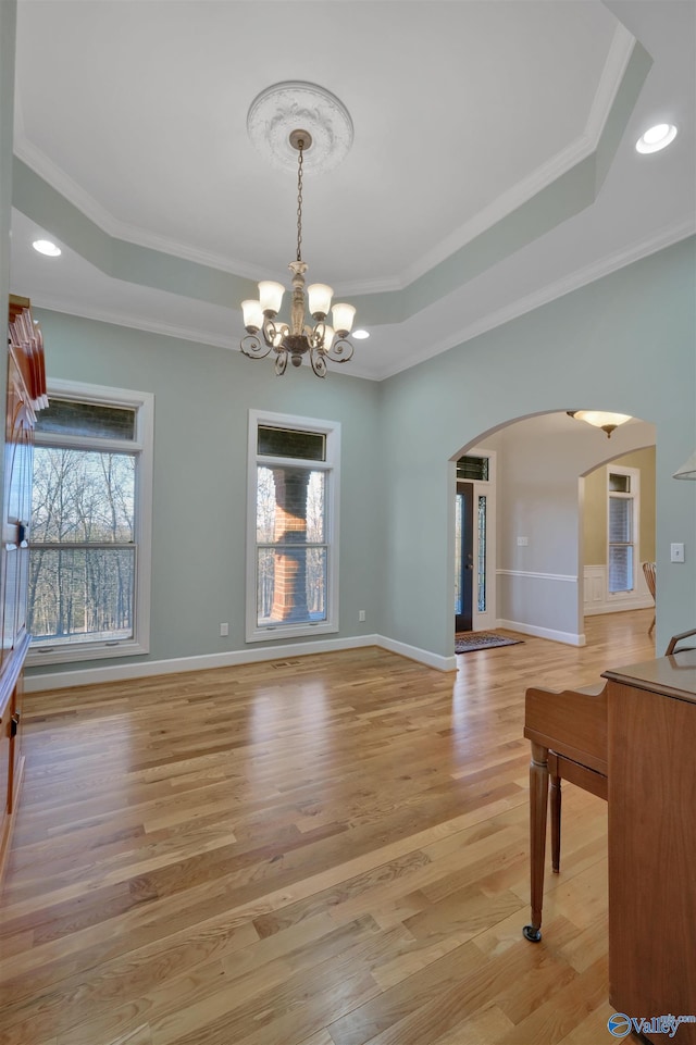 interior space featuring light wood-type flooring, a raised ceiling, an inviting chandelier, and ornamental molding