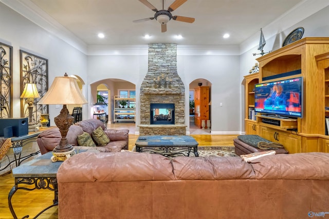 living room with ceiling fan, light hardwood / wood-style flooring, crown molding, and a stone fireplace