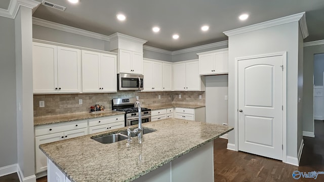 kitchen featuring light stone counters, visible vents, appliances with stainless steel finishes, ornamental molding, and an island with sink