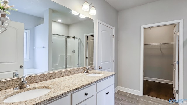 full bath with a stall shower, a sink, baseboards, and double vanity