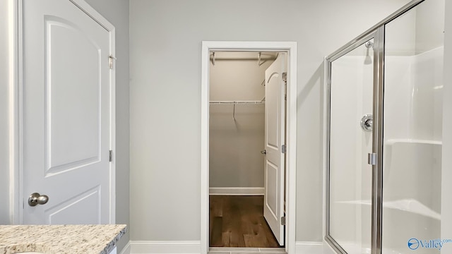 bathroom with wood finished floors, a shower stall, baseboards, and a spacious closet