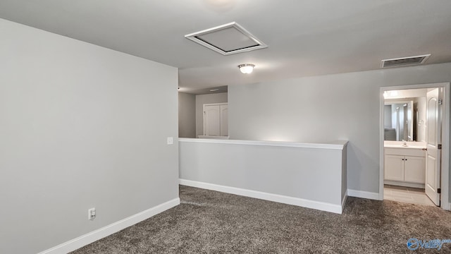 carpeted spare room featuring visible vents, a sink, attic access, and baseboards