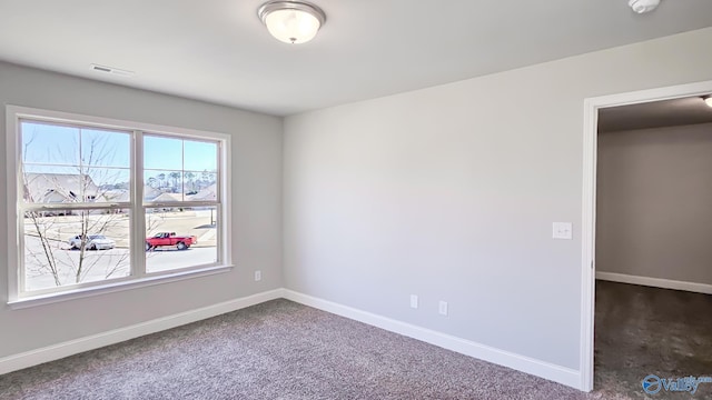 unfurnished room featuring dark colored carpet, visible vents, and baseboards