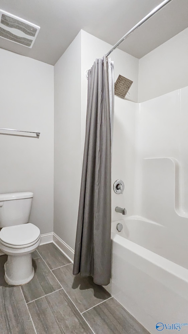 bathroom featuring toilet, shower / bath combo, visible vents, and baseboards