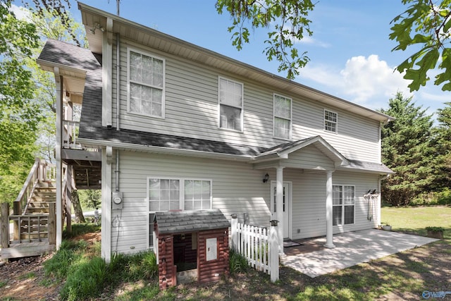 rear view of property featuring roof with shingles, fence, a yard, a patio, and stairway