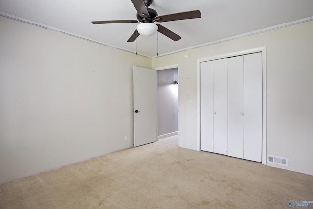 unfurnished bedroom featuring light carpet, ceiling fan, a closet, and crown molding