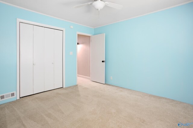 unfurnished bedroom featuring ceiling fan, light carpet, a closet, and ornamental molding