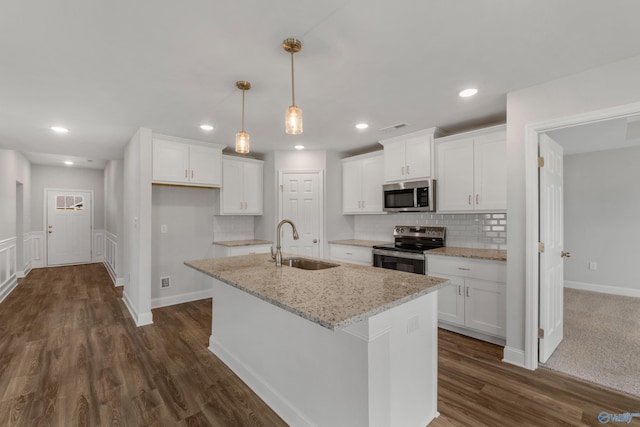 kitchen with light stone countertops, stainless steel appliances, an island with sink, and white cabinets