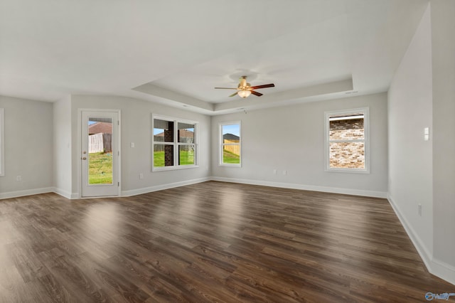 spare room with dark wood-type flooring, a healthy amount of sunlight, and a tray ceiling