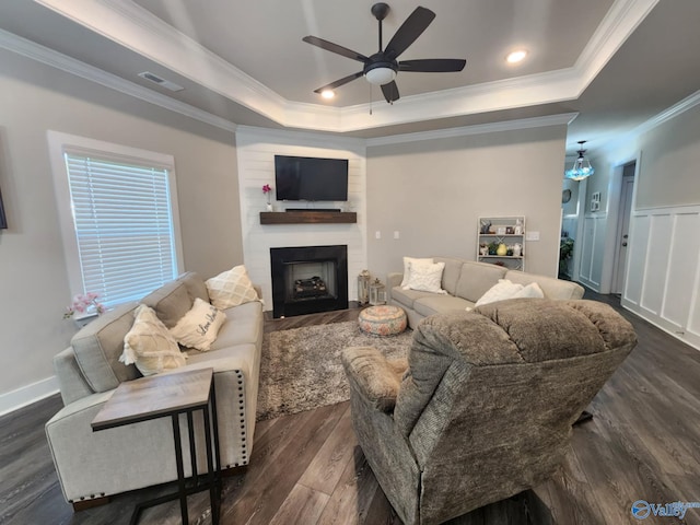 living room featuring dark wood-type flooring, a tray ceiling, ornamental molding, a fireplace, and ceiling fan