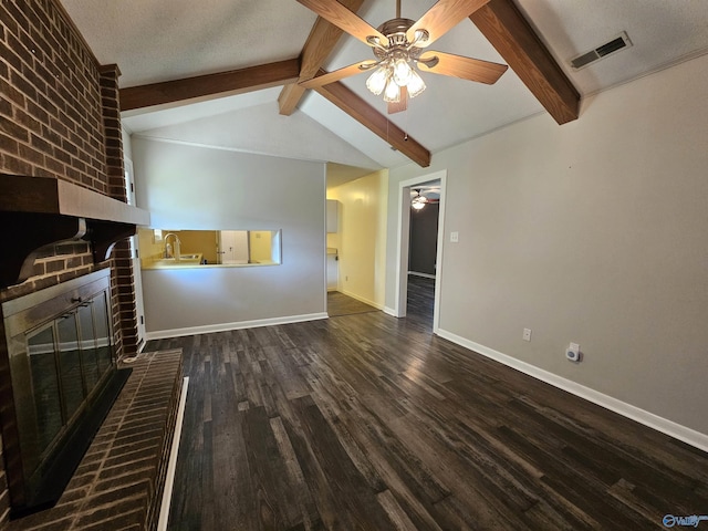 unfurnished living room featuring dark wood-type flooring, ceiling fan, lofted ceiling with beams, a textured ceiling, and a brick fireplace