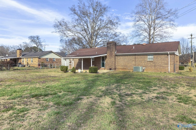 rear view of property with a yard, brick siding, a chimney, and fence