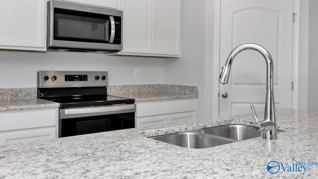 kitchen with white cabinets, stainless steel appliances, light stone counters, and sink