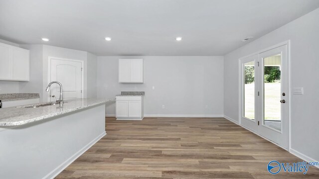 kitchen featuring light stone counters, sink, white cabinets, and light hardwood / wood-style floors