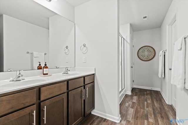 full bath featuring wood finished floors, a shower stall, double vanity, and baseboards