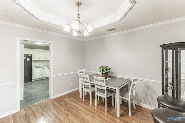 dining room featuring an inviting chandelier, a raised ceiling, ornamental molding, and light tile patterned floors