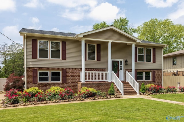 bi-level home with a porch, brick siding, a shingled roof, and a front yard