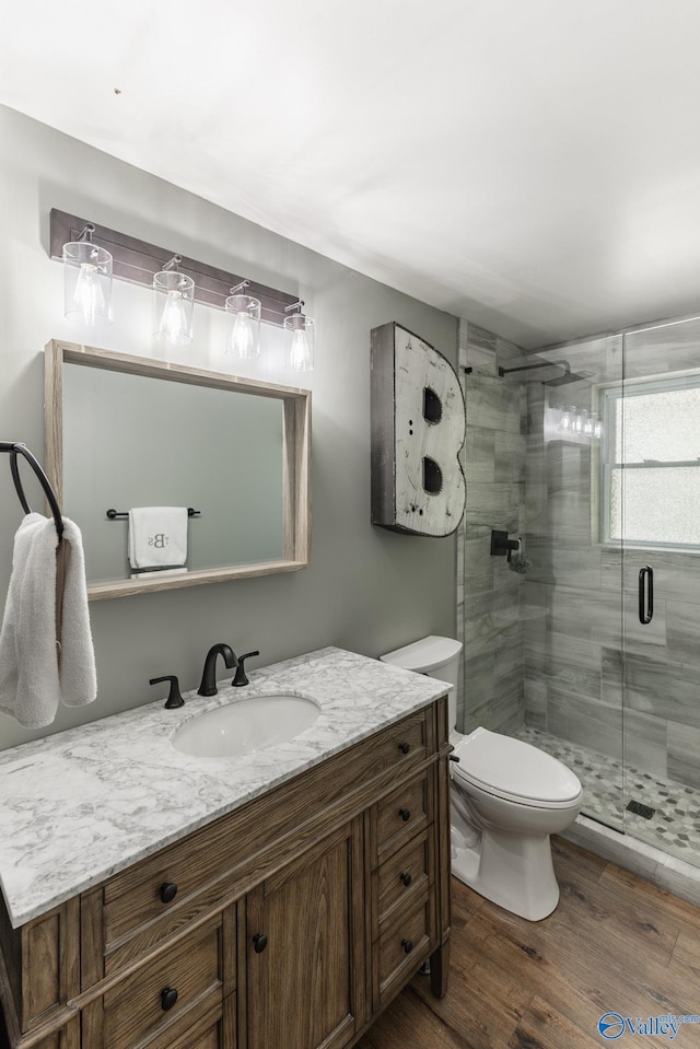 bathroom with wood finished floors, a stall shower, toilet, and vanity