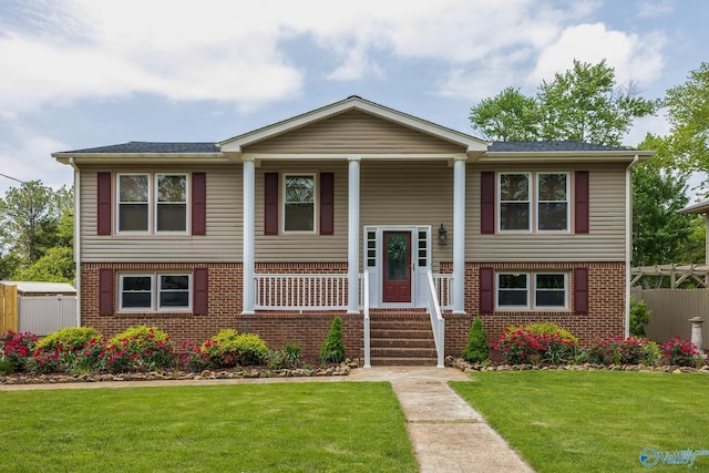 raised ranch featuring covered porch, brick siding, and a front lawn