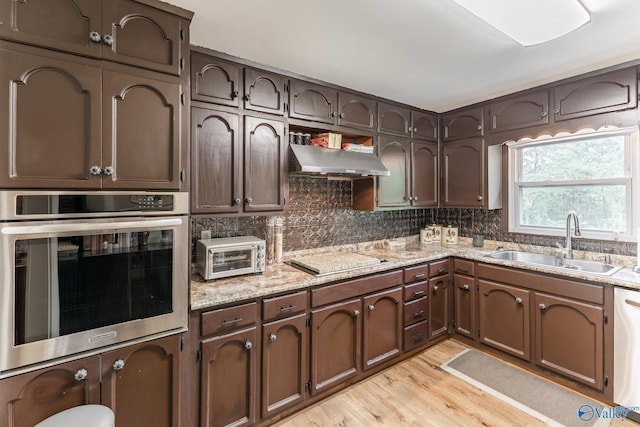 kitchen featuring backsplash, appliances with stainless steel finishes, a sink, a toaster, and light wood-style floors