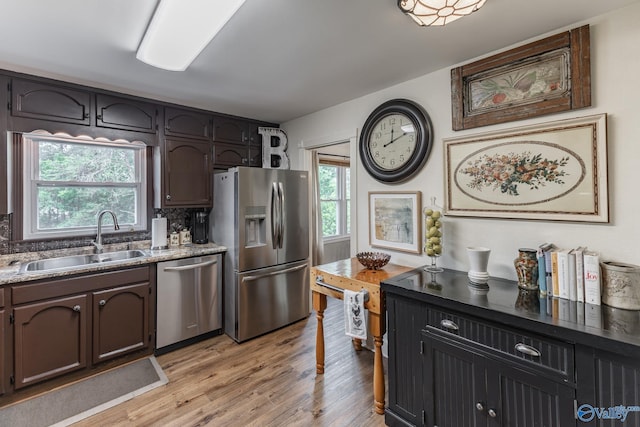 kitchen featuring light wood-style floors, a sink, decorative backsplash, and appliances with stainless steel finishes