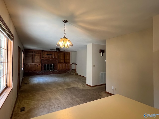 unfurnished living room featuring dark carpet, ceiling fan, a brick fireplace, and plenty of natural light