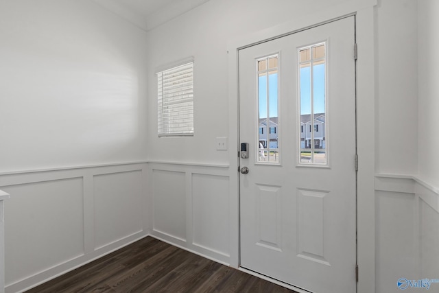 doorway to outside featuring crown molding, a decorative wall, dark wood-style floors, and wainscoting