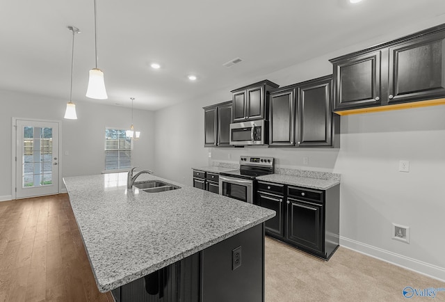 kitchen with visible vents, a kitchen island with sink, a sink, dark cabinetry, and stainless steel appliances