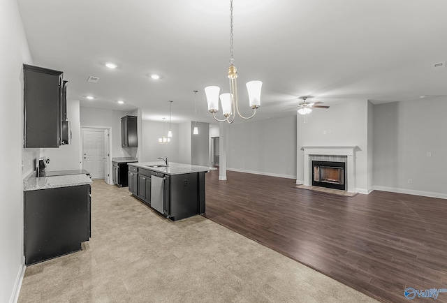 kitchen featuring dark cabinetry, a kitchen island with sink, a sink, appliances with stainless steel finishes, and a tiled fireplace