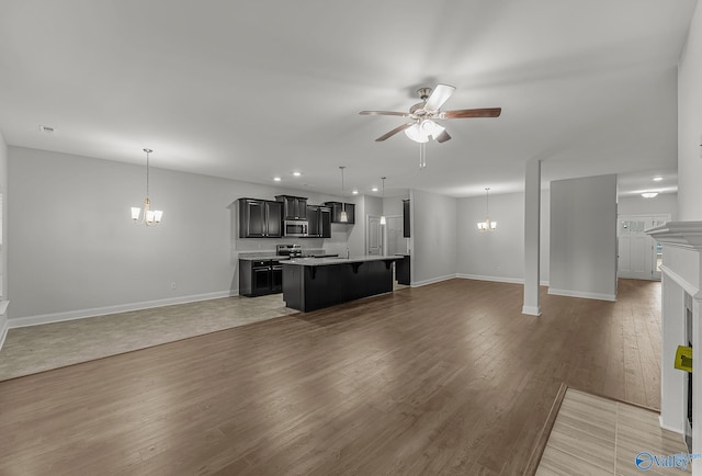 living room with recessed lighting, light wood-type flooring, baseboards, and ceiling fan with notable chandelier