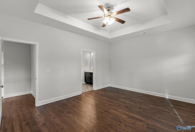 unfurnished room featuring a ceiling fan, baseboards, visible vents, a tray ceiling, and dark wood-style flooring