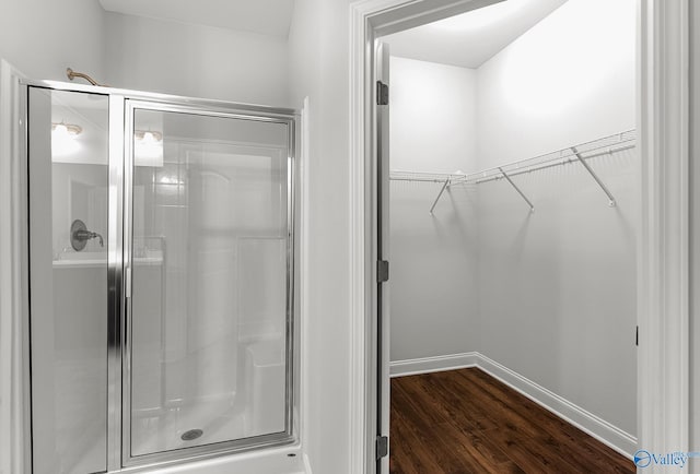 bathroom featuring a walk in closet, wood finished floors, a stall shower, and baseboards