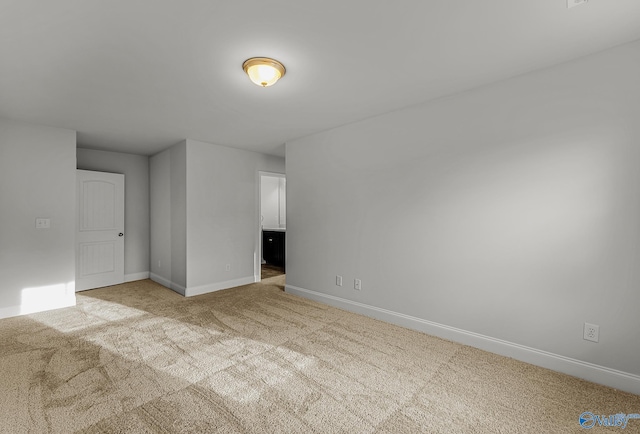 spare room featuring light colored carpet and baseboards