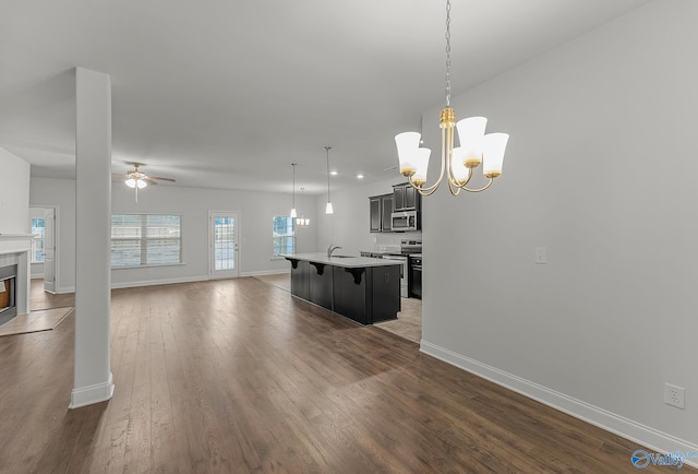 kitchen featuring ceiling fan with notable chandelier, open floor plan, stainless steel appliances, a breakfast bar area, and dark wood-style flooring