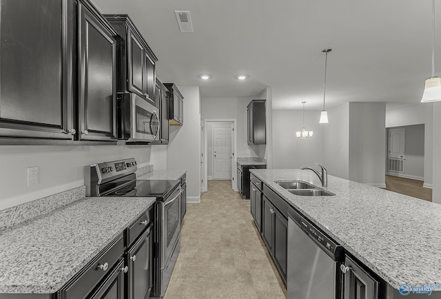 kitchen with visible vents, an island with sink, appliances with stainless steel finishes, dark cabinetry, and a sink