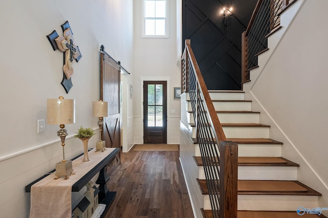 foyer entrance featuring dark hardwood / wood-style floors, a towering ceiling, a healthy amount of sunlight, and a barn door