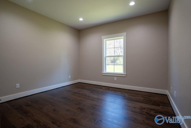 empty room featuring dark wood finished floors, visible vents, recessed lighting, and baseboards