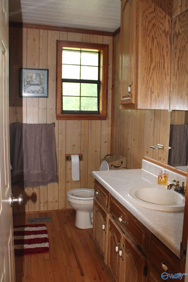 bathroom with wooden walls, wood-type flooring, toilet, and vanity