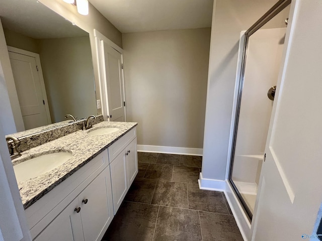 full bathroom featuring double vanity, a stall shower, baseboards, and a sink