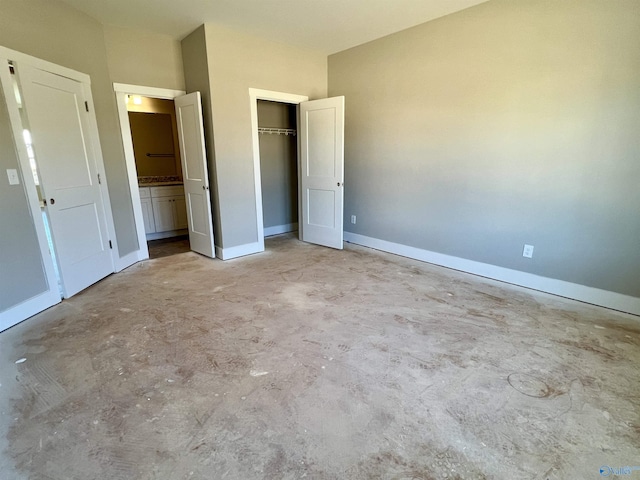 unfurnished bedroom featuring ensuite bath, concrete floors, baseboards, and a closet