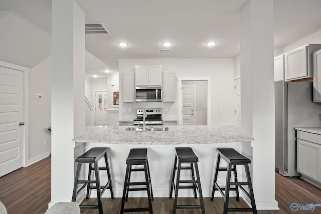 kitchen with appliances with stainless steel finishes, sink, white cabinets, light stone countertops, and dark wood-type flooring