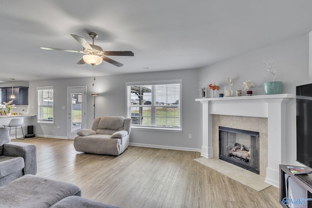 living room featuring ceiling fan, a tile fireplace, and light wood-type flooring